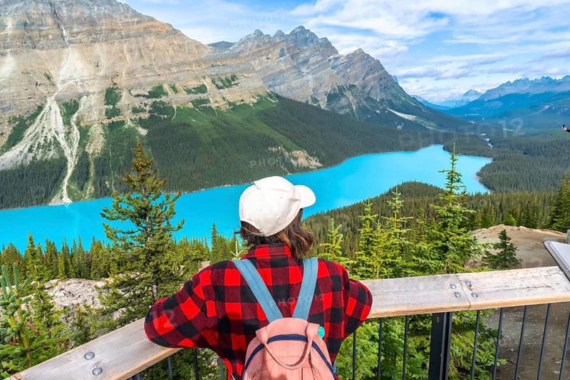 Female tourist with a backpack admiring the stunning turquoise waters of peyto lake, framed by the majestic canadian rockies in banff national park, alberta