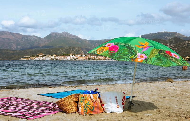 Sunshade and swimwear on the beach or Plage de la Roya, in the back Saint-Florent on the Gulf of Saint-Florent in the Mediterranean, Haute-Corse, Corsica