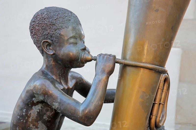 Sculpture boy with tuba by Guido Messer 1991, modern art, bronze sculpture, playing music, tuba, brass instrument, sitting, jack, big cheeks, bubbles, size comparison, big, small, half-timbered house, music school, Waldenbuch, Baden-Württemberg, Germany