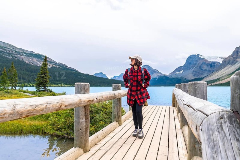 Female tourist enjoying breathtaking view of turquoise bow lake and surrounding mountains while walking on wooden bridge in banff national park, canadian rockies, alberta, canada