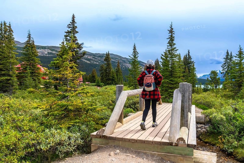 Female tourist with backpack walking on a wooden bridge and enjoying the landscape of bow lake and num ti jah lodge in the canadian rockies, banff national park, alberta, canada