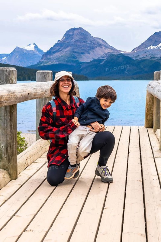 Mother happily holds her son on a wooden bridge, enjoying the stunning turquoise waters of bow lake and the majestic mountains of banff national park in the canadian rockies