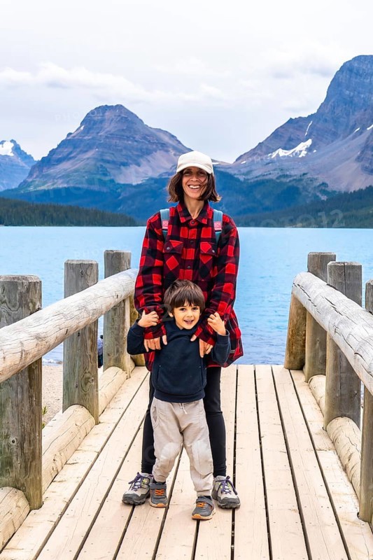Smiling mother and son embracing the stunning scenery of turquoise bow lake and surrounding mountains in banff national park, capturing a beautiful family moment in nature