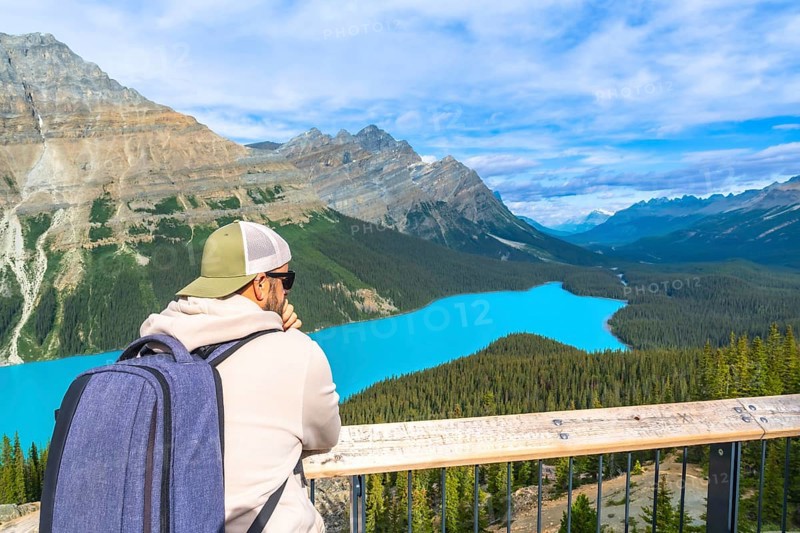 Tourist with backpack is enjoying the breathtaking panoramic view of the turquoise peyto lake and surrounding canadian rockies in banff national park, alberta, on a beautiful sunny day