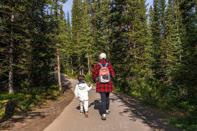 Mother and child holding hands, enjoying a leisurely hike along a paved path, surrounded by the lush green trees of banff national park in the canadian rockies