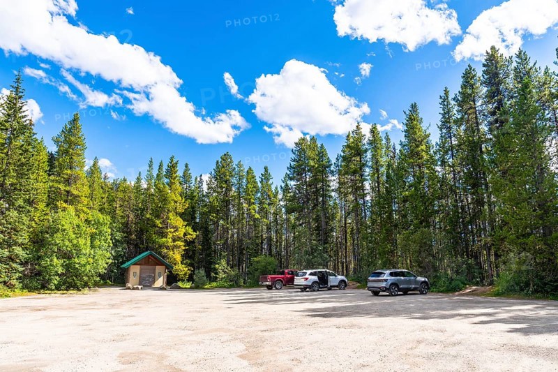 Herbert lake parking lot nestled in lush pine forest under a vibrant blue sky with fluffy clouds, providing a serene base for exploring banff national park's beauty