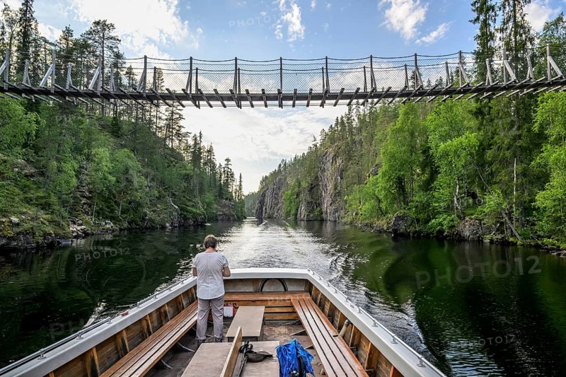 A boat sails on a calm lake under a suspension bridge between wooded banks, Julmy Ölkky, Hossq National Park, Irni, Northern Ostrobothnia, Finland