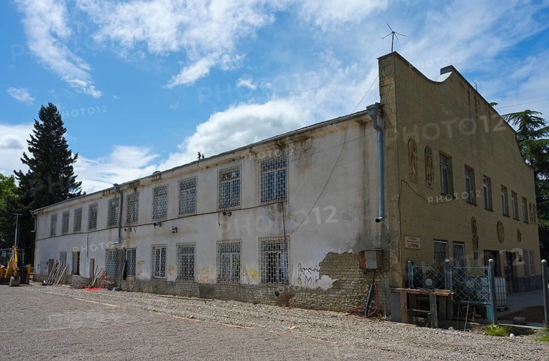 Old, dilapidated building with lattice windows under cloudy sky, excavator in the foreground, Evangelical Lutheran church built in 1854, which later became a cinema and has been a sports school since 1989, Bolnissi, Katharinenfeld, founded by Caucasian German settlers, Lower Kartli region, Kwemo Kartli, Georgia