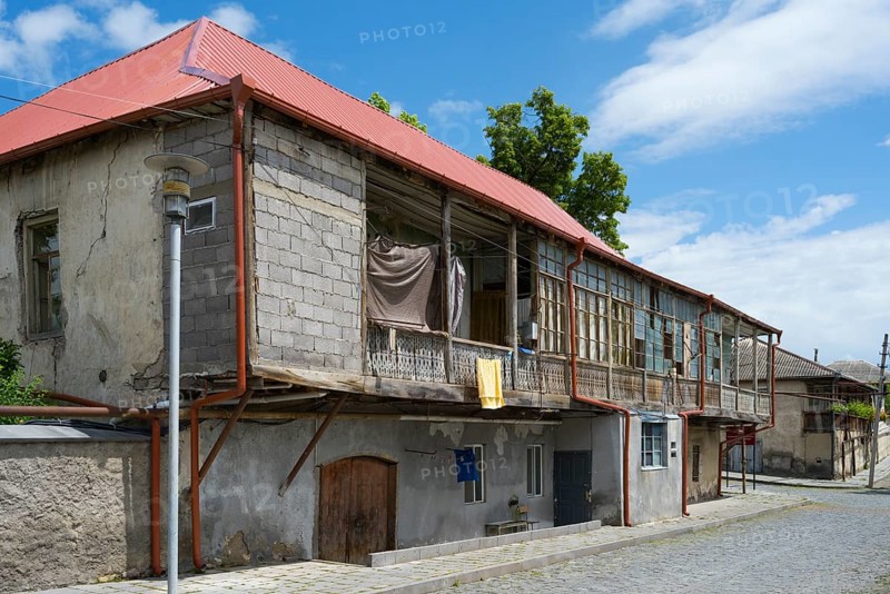 An old, rustic building with a dilapidated state and wooden veranda under a clear blue sky, traditional German residential building, Nikolaistraße 30, Bolnissi, Katharinenfeld, founded by Caucasian German settlers, Lower Kartli region, Kwemo Kartli, Georgia