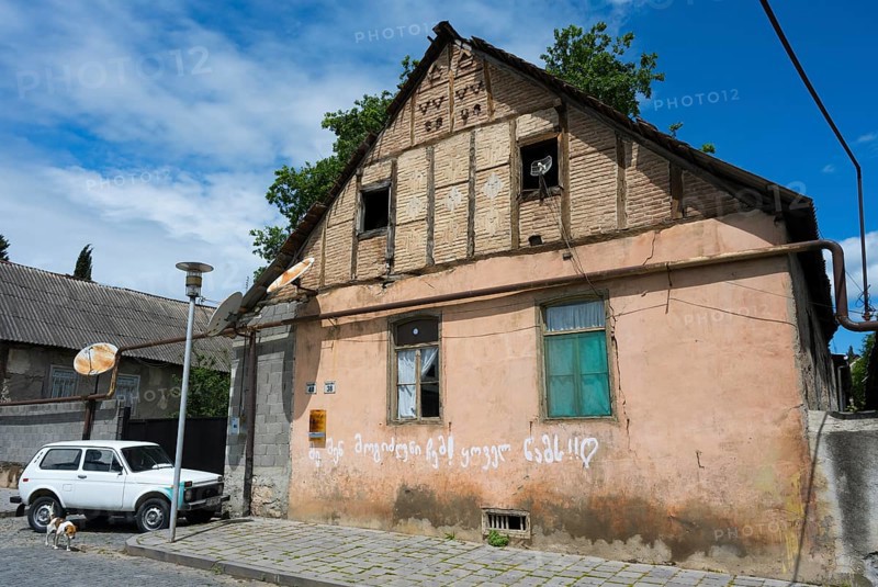A dilapidated house with leaning antennas and graffiti, next to a parked car under cloudy sky, traditional German residential building, Nikolaistraße 38-40, Bolnissi, Katharinenfeld, founded by Caucasian German settlers, Lower Kartli region, Kwemo Kartli, Georgia