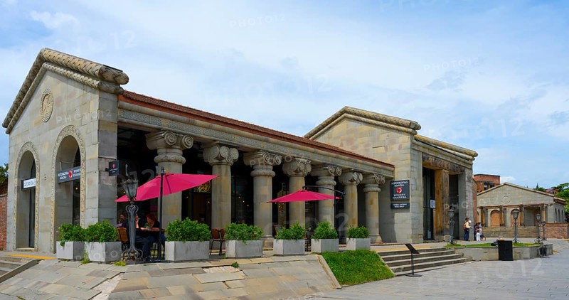 Historic stone building with ancient columns and red umbrellas under cloudy sky, Mtskheta, Mtskheta, Mtskheta-Mtianeti region, Georgia