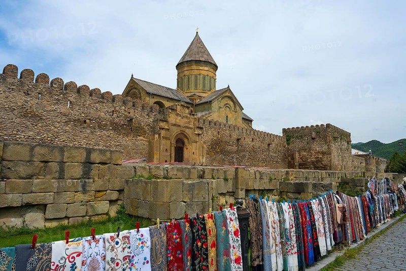 Stone fortress with monastery in the background, lots of colorful fabrics hung in front of it, Svetitskhoveli Cathedral, Svetitskhoveli, UNESCO World Heritage, Mtskheta, Mtskheta, Mtskheta, Mtskheta-Mtianeti region, Georgia