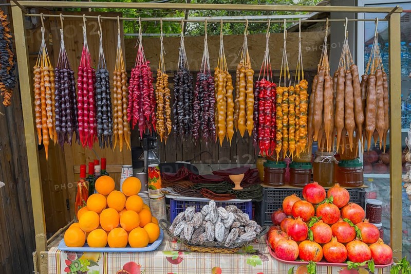 Colourful fruit and candy display with hanging goodies, Churchkhela, Georgian confections, 'Georgian Snickers', in front oranges, dried fruits and pomegranates, Mtskheta, Mtskheta, Mtskheta, Mtskheta, Mtskheta-Mtianeti region, Georgia