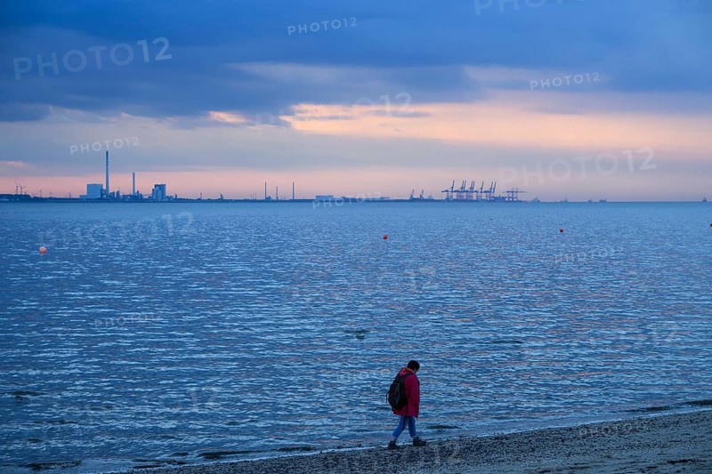 Person on the beach with a view of the sea and industrial areas in Wilhelmshafen right Jade-Weser Port, blue-orange twilight, Eckwarderhörne, Butjadingen, Lower Saxony, Germany