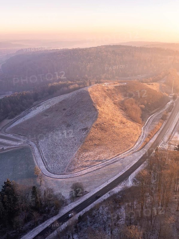 Aerial view of a hill in morning light with snow-covered roads and surrounding forest, future PV construction on old deposit, Lindenrain industrial park, Calw, Germany