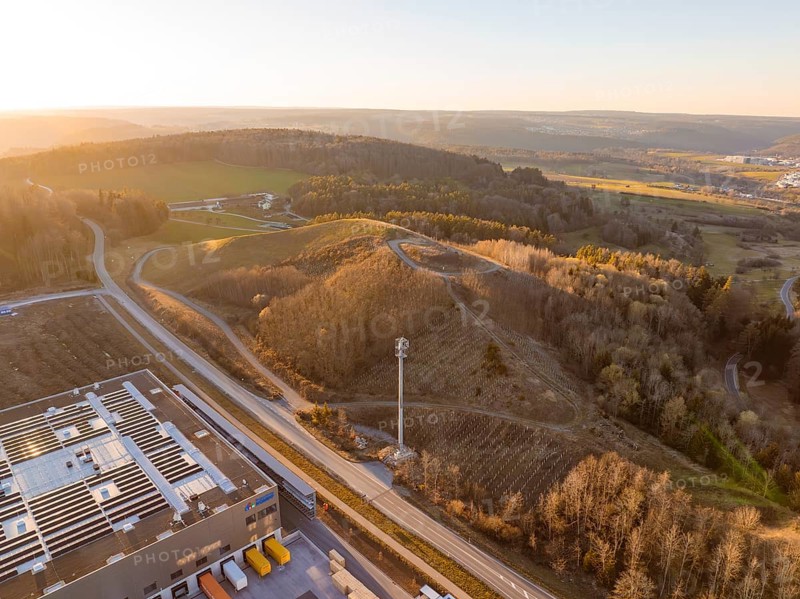 Telecommunication tower over hilly landscape and industrial buildings in the evening light, future PV construction on old deposit, Lindenrain industrial park, Calw, Germany
