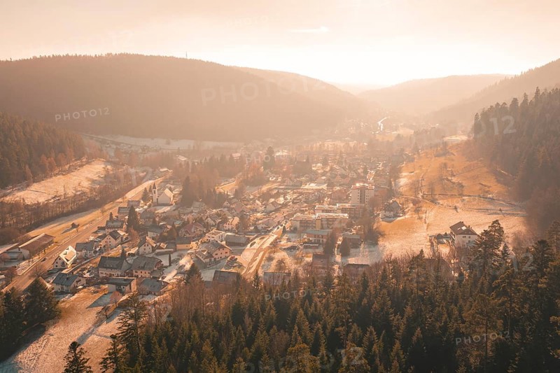 Panoramic view of a village with snow-covered roofs surrounded by forests and hills in the evening light, Enzklösterle, Calw district, Germany