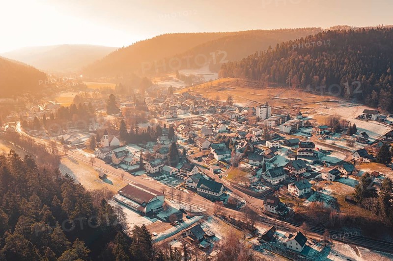 Extensive aerial view of a valley with snowy houses surrounded by mountains and warm sunset light, Enzklösterle, Calw district, Germany