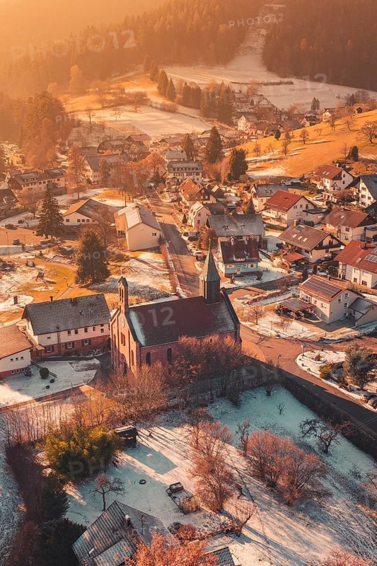 Snowy village with central church, warm sunlight bathes the surrounding area in golden tones, Enzklösterle, Calw district, Germany