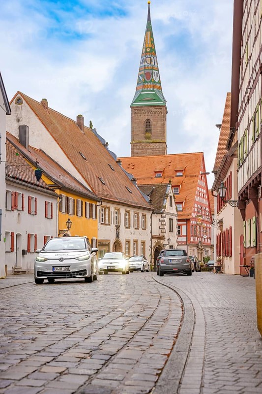 Historic old town with cobblestones and colorful houses, a church tower in the background, ID3, deer e-car sharing, Germany