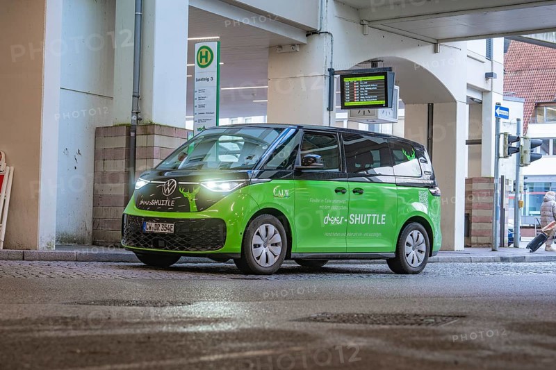 Green VW shuttle at a bus stop, modern urban atmosphere, Deer E-Mobility Shuttle Service, Calw, Germany