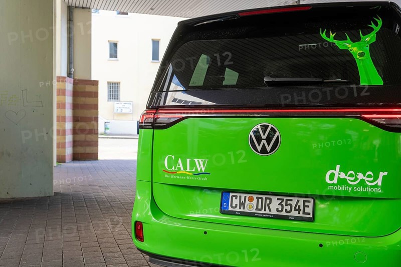 Volkswagen in green with lettering on the back in an urban environment, Deer E-Mobility Shuttle Service, Calw, Germany