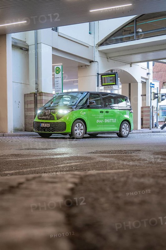 Green shuttle goes around a bend in an urban area, busy atmosphere, Deer E-Mobility Shuttle Service, Calw, Germany
