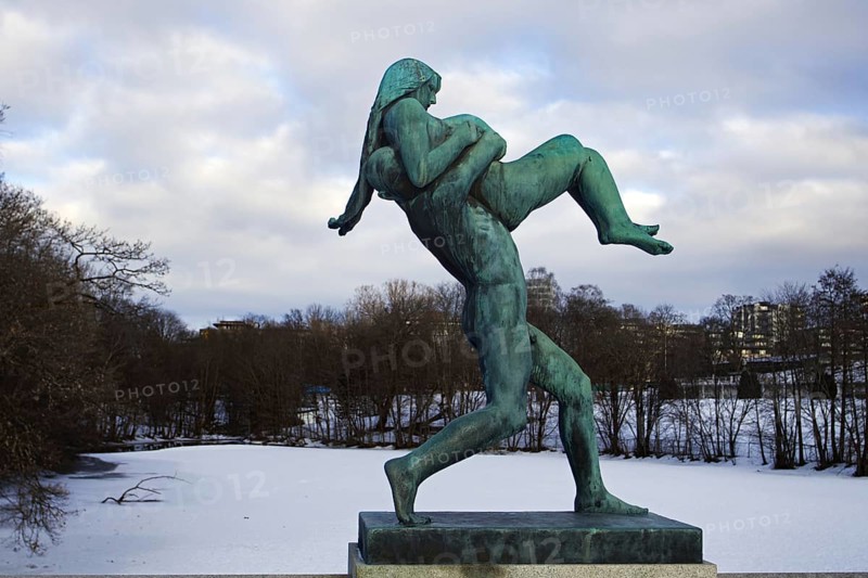 Bronze statue of a man carrying a woman. Winter landscape, icy river in the background, Vigeland sculpture park Oslo Norway