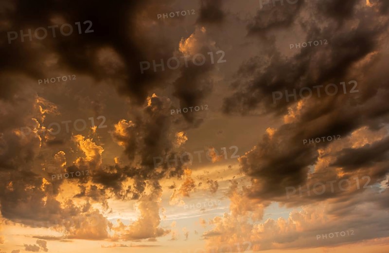 A brilliant sunset casts warm colors across a cheerful meadow. Dark clouds dominate the sky, while golden light penetrates and creates a dramatic and peaceful atmosphere. Bas Rhin, Alsace, France