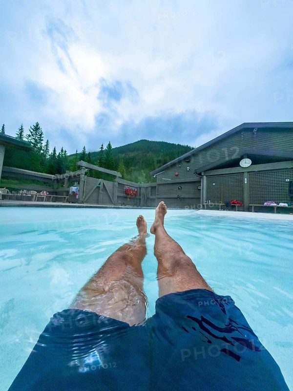 Tourist relaxing in the miette hot springs, surrounded by the breathtaking beauty of jasper national park, with legs extended in the turquoise water