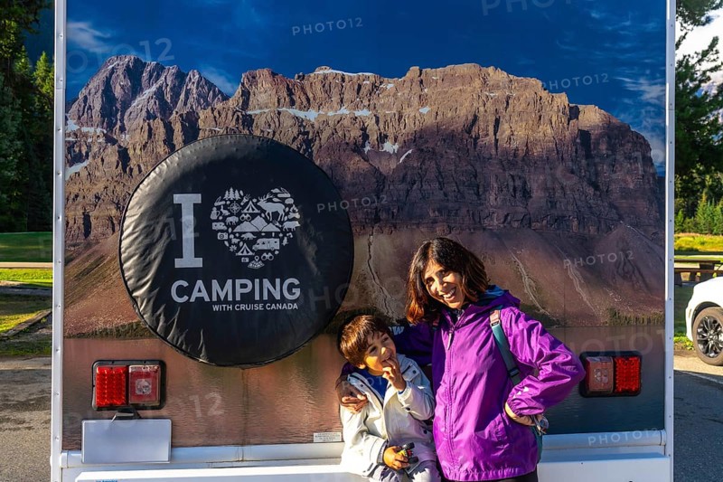 Mother and son posing happily in front of their rv, featuring a large i love camping graphic and a stunning view of mount robson in the canadian rockies