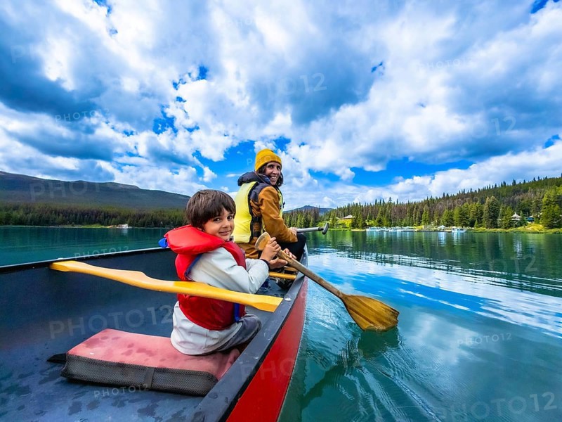 Father and son are paddling a canoe on beautiful maligne lake in jasper national park, alberta, canada, enjoying the stunning scenery of mountains and forests on a sunny day