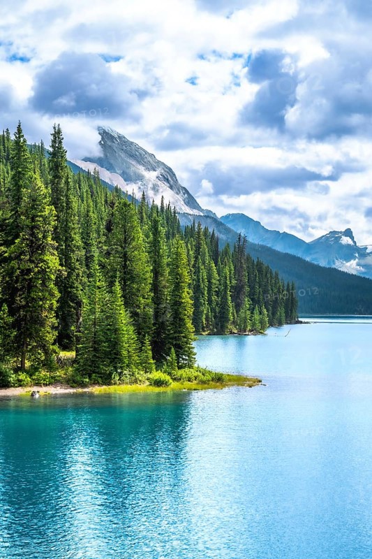 Turquoise maligne lake reflecting a cloudy sky, surrounded by lush pine forests and rocky mountains in jasper national park, a breathtaking unesco world heritage site