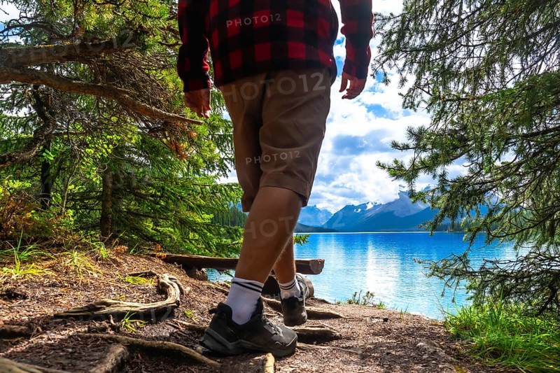 Hiker walking along a forest path toward maligne lake's turquoise waters, framed by a mountain range and a cloudy sky in jasper national park, alberta, canada