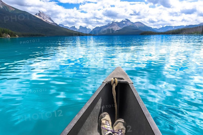 Hiking boots inside a canoe navigating the turquoise waters of maligne lake with its surrounding mountains and forests in jasper national park in the canadian rockies, alberta, canada