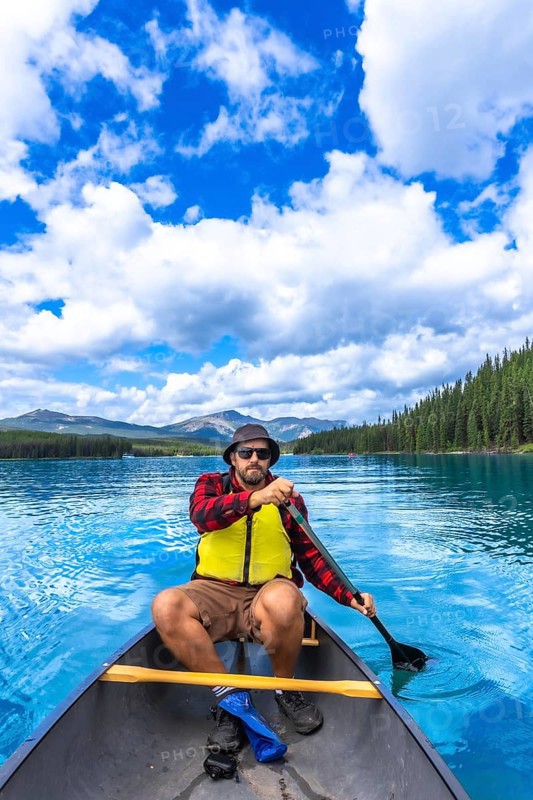 Tourist paddling a canoe in maligne lake under a beautiful cloudy sky, enjoying the turquoise water and surrounding nature of jasper national park in the canadian rockies