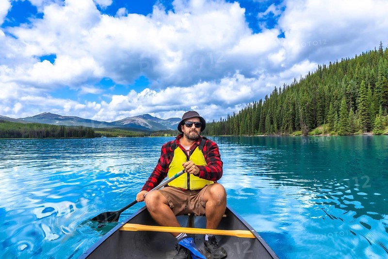 Tourist paddling a canoe on turquoise maligne lake with spirit island in the distance, enjoying the breathtaking scenery of jasper national park in the canadian rockies