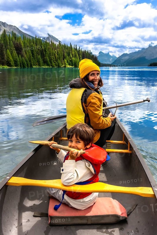 Mother and son paddling a canoe on maligne lake's turquoise waters, surrounded by mountains and pine trees in jasper national park on a sunny summer day