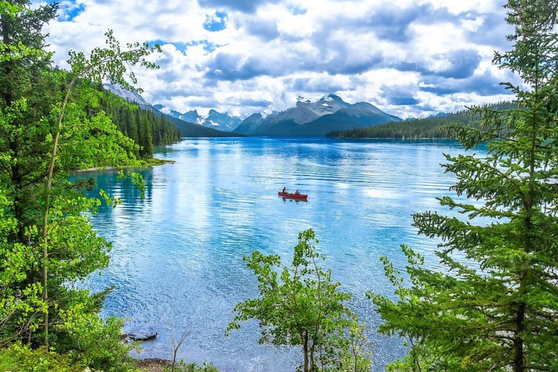 Two tourists enjoying a canoe ride on the turquoise waters of maligne lake, surrounded by lush trees and the majestic canadian rockies in jasper national park