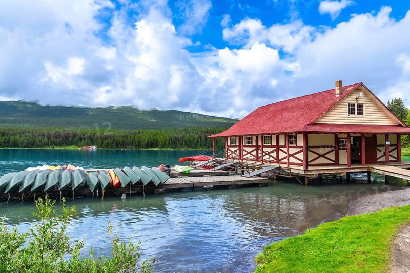 Colorful canoes and kayaks resting on a wooden dock in front of a boathouse on the beautiful maligne lake in jasper national park, with the canadian rockies in the background under a summer sky