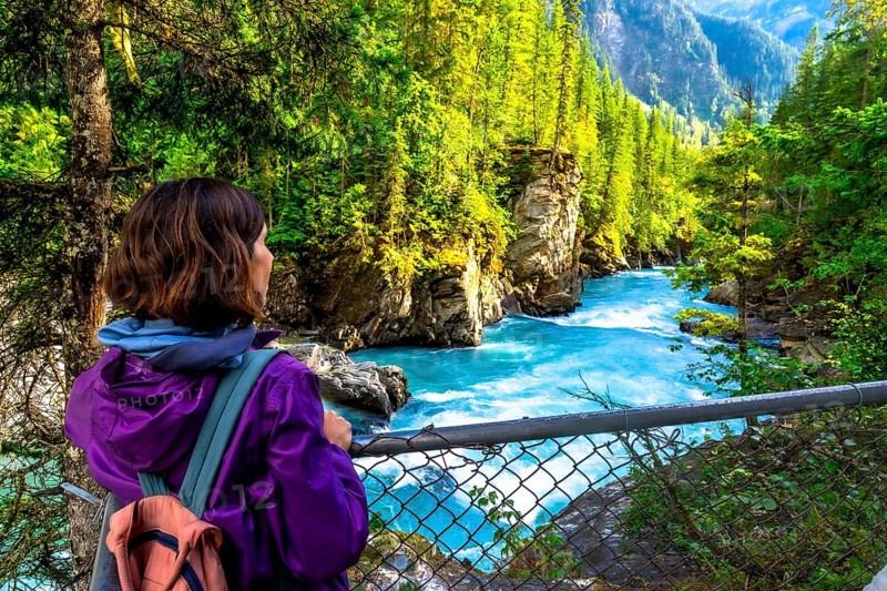 Female hiker enjoying the breathtaking turquoise waters of the fraser river cascading through the scenic canyon at overlander falls in mount robson provincial park, british columbia, canada
