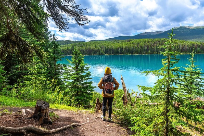 Female hiker with a backpack admiring the stunning turquoise waters of maligne lake, surrounded by lush evergreens and majestic mountains in jasper national park