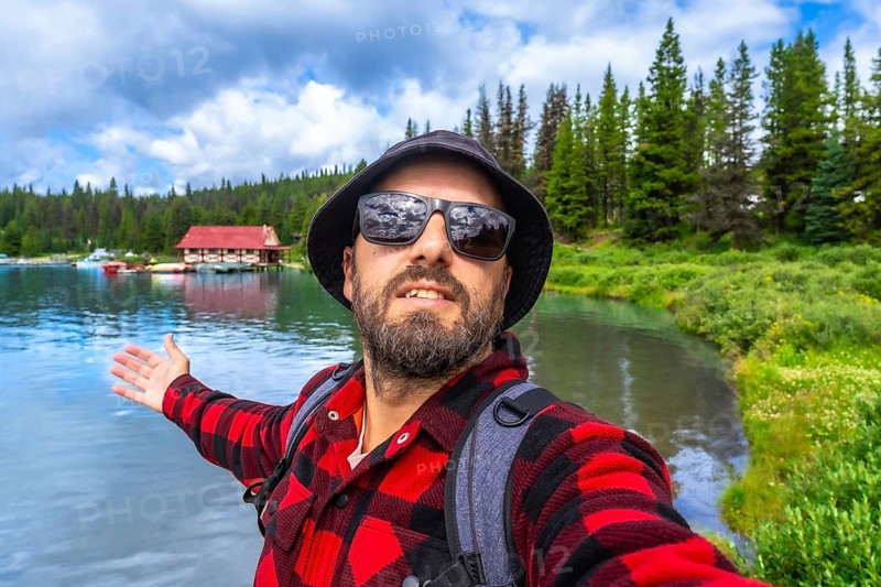Happy tourist showing with open arms the beautiful maligne lake with the boathouse at jasper national park during a sunny summer day in alberta canada