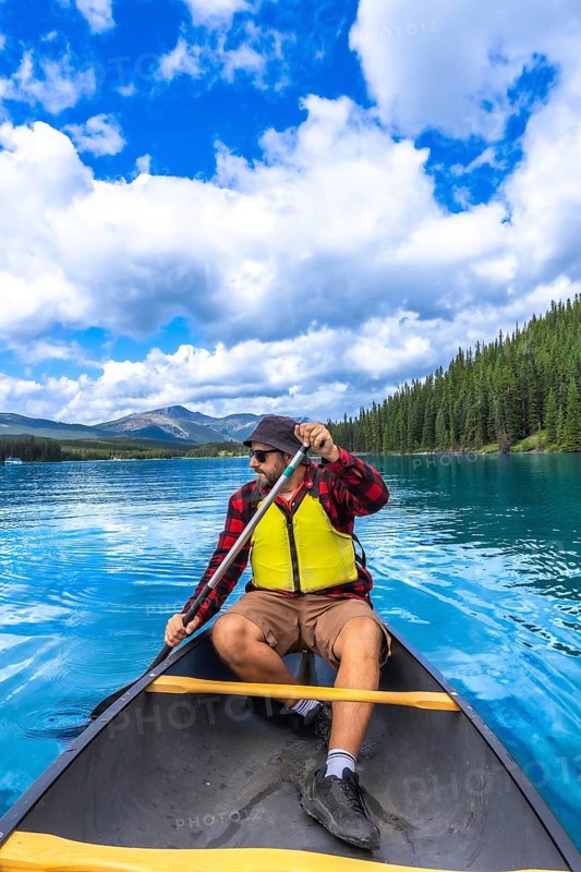 Tourist wearing sunglasses and life jacket paddling a canoe on beautiful maligne lake in jasper national park with blue sky, clouds, mountains, and forest in the background