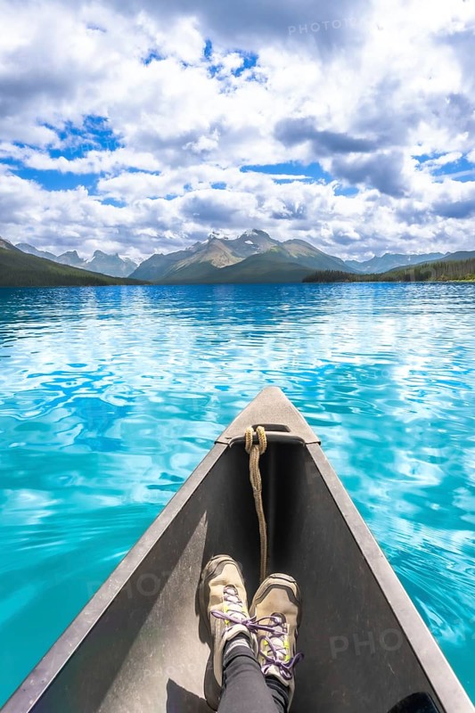 Tourist enjoys stunning view of turquoise water and mountain range while paddling canoe on maligne lake in jasper national park on a beautiful summer day