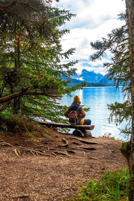 Hiker sitting on a wooden bench, admiring the breathtaking view of maligne lake and the surrounding mountains in jasper national park, alberta, canada, enjoying the tranquility of nature