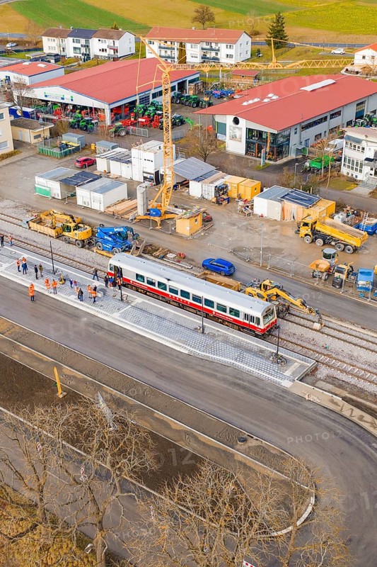 A train passes a large construction site with workers and a crane, historic event, first test run with a passenger train on the Hermann tracks, Hesse Railway since 1988, Calw district, Germany