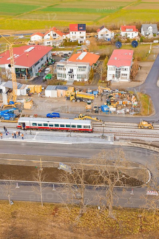 A train passes a construction site with numerous buildings and a crane in a rural area, historic event, first test run with a passenger train on the Hermann tracks, Hesse Railway since 1988, Calw district, Germany