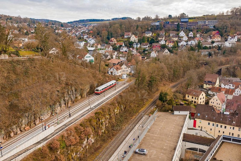 A train travels through a hilly area with urban houses and winter trees under a cloudy sky, historical event, first test run with a passenger train on the Hermann tracks, Hesse Railway since 1988, Calw, Calw district, Germany