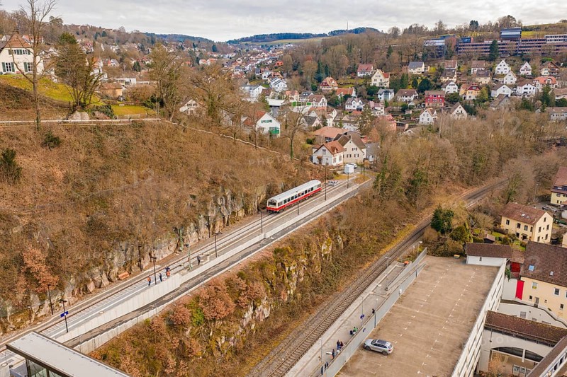 A train moves through an urban environment with hills and houses, surrounded by winter vegetation and clouds, historic event, first test run with a passenger train on the Hermann tracks, Hesse Railway since 1988, Calw, Calw district, Germany
